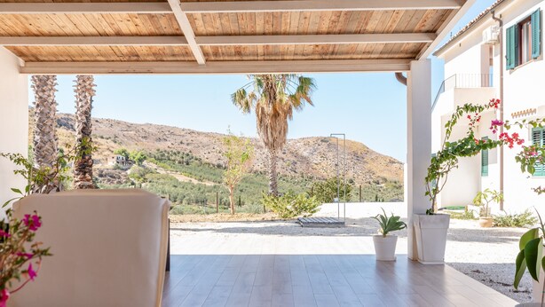 A covered outdoor seating area with a view of a mountainous landscape, potted plants, and a wooden table. - Room 'Monte Suso' with sea view, shared terrace and air conditioning (Montallegro)