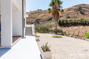A modern building with a white exterior, a concrete pathway leading to a set of stairs, and a gravel area with potted plants and a palm tree. - Room 'Monte Suso' with sea view, shared terrace and air conditioning (Montallegro)