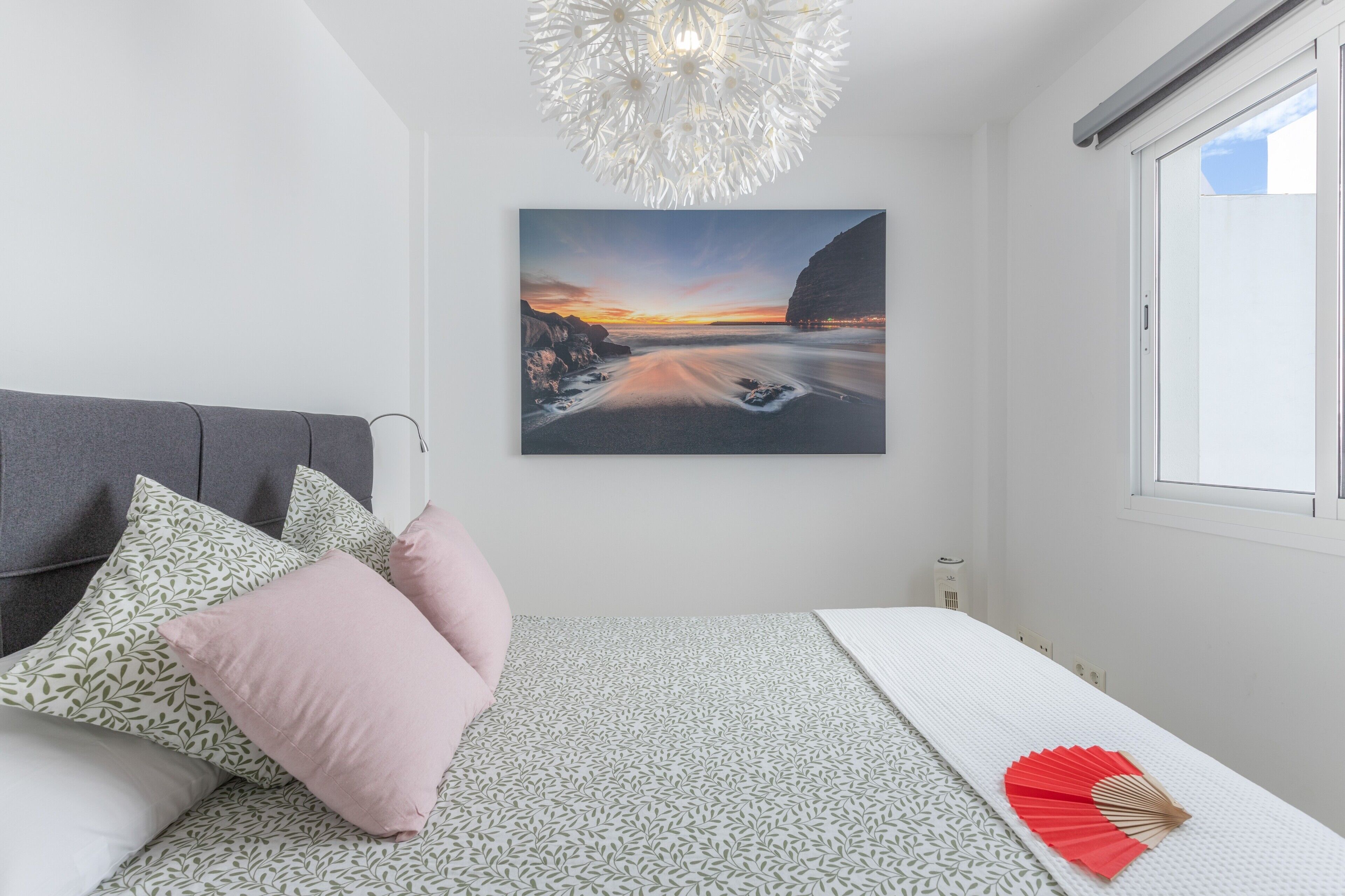 A bedroom with a bed, pillows, a wall-mounted picture, a window, and a ceiling light fixture.
