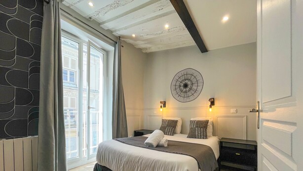 A bedroom with a bed, a large window, a wall-mounted decorative piece, and a door. - UrbanFlat 44 - Pretty 2 Bedroom Flat in Paris near metro station (París)