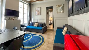 A modern living room with a sofa, a red bench, a dining table, and a TV. - UrbanFlat 44 - Pretty 2 Bedroom Flat in Paris near metro station (París)
