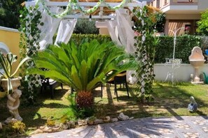 A garden with a large green plant, white decorative arches, and a tiled patio area.