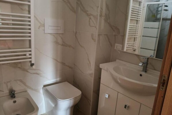 A bathroom with a toilet, bidet, sink, and mirror.