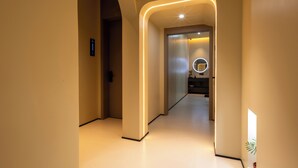 Un pasillo moderno con una pared curva iluminada, un ascensor a la vista y una pequeña planta en maceta.