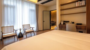 Una habitación de hotel con una cama grande, dos sillas, un escritorio con una computadora y una estantería.