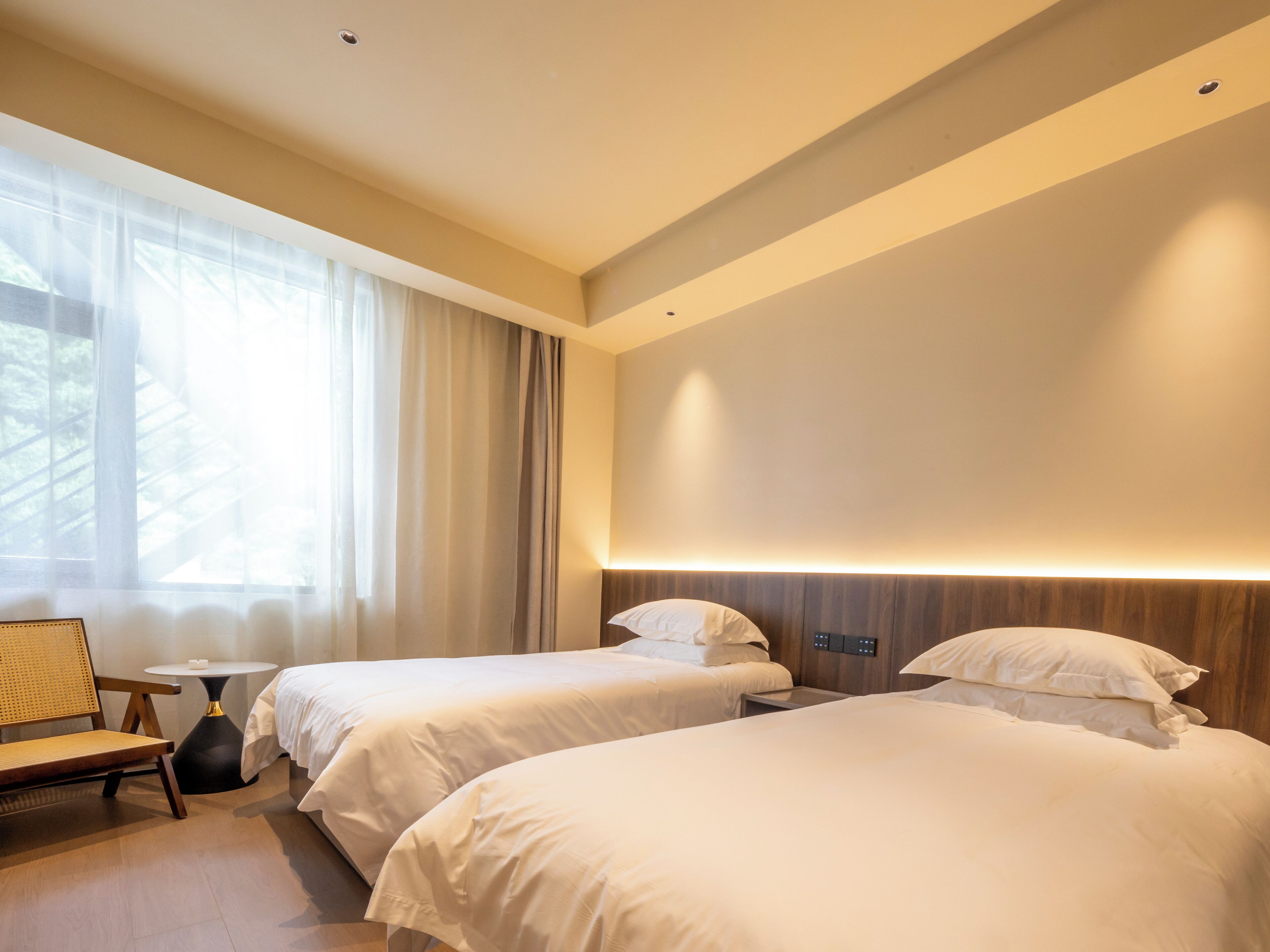 A modern hotel room with two beds, a small table, and a chair.