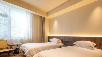 A modern hotel room with two beds, a small table, and a chair.