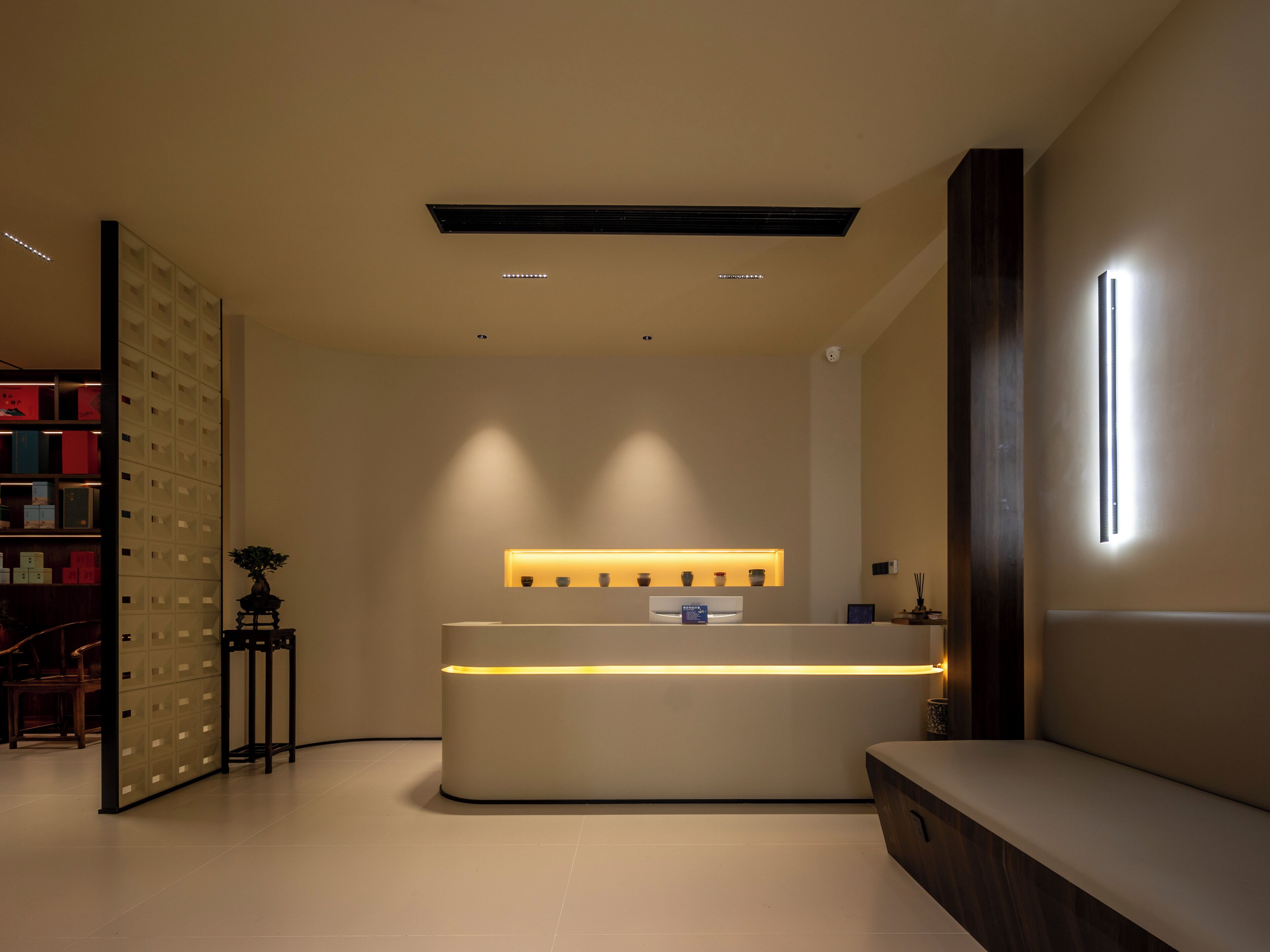 A modern reception desk with a built-in light, a wall-mounted security camera, and a shelf with decorative items.