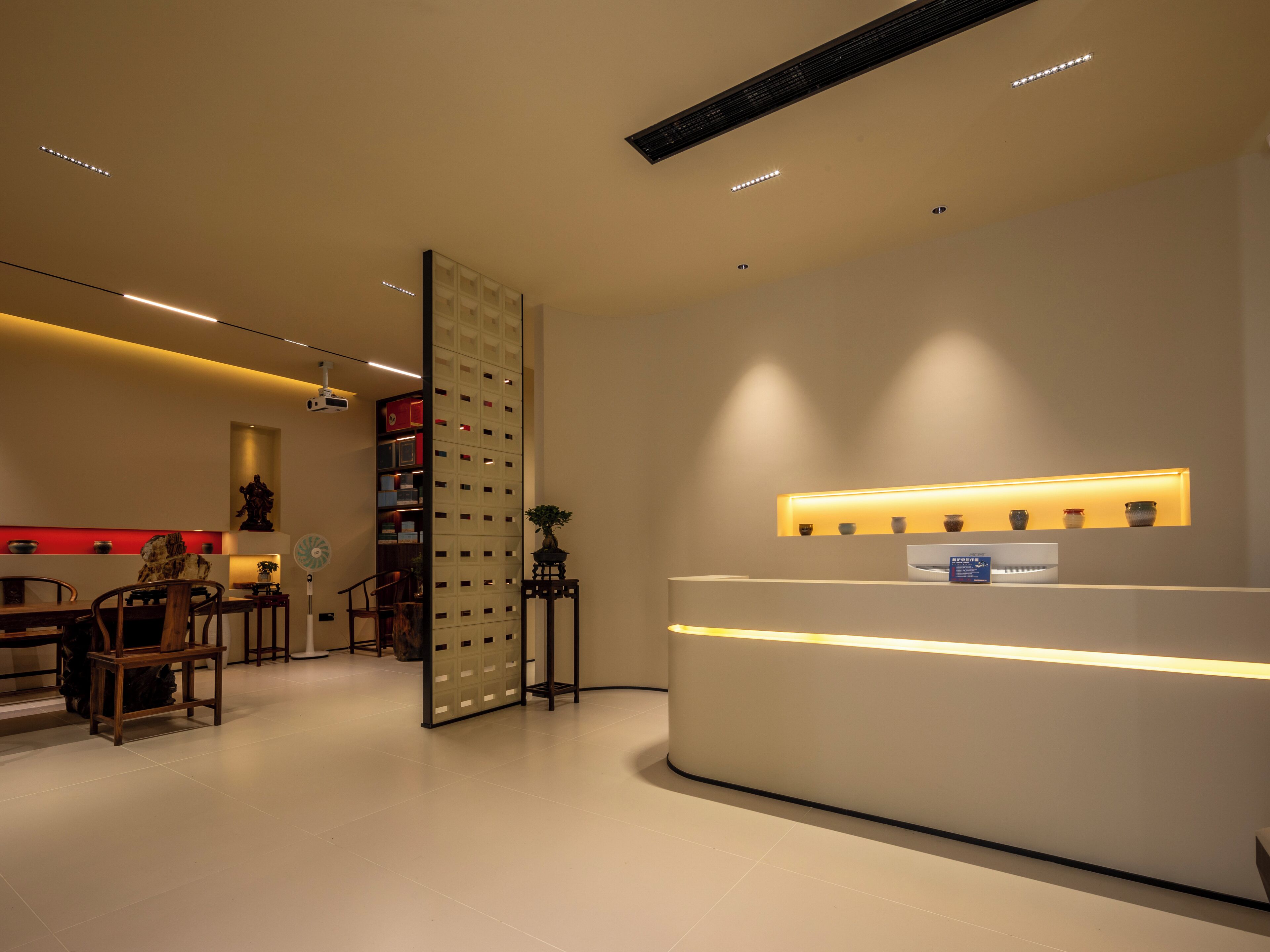 A modern reception area with a reception desk, a seating area with chairs, a decorative plant, and a wall-mounted shelf with small items.