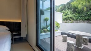 Habitación de hotel moderna con un ventanal grande, una cama, una mesita y vistas a una ladera verde y exuberante.