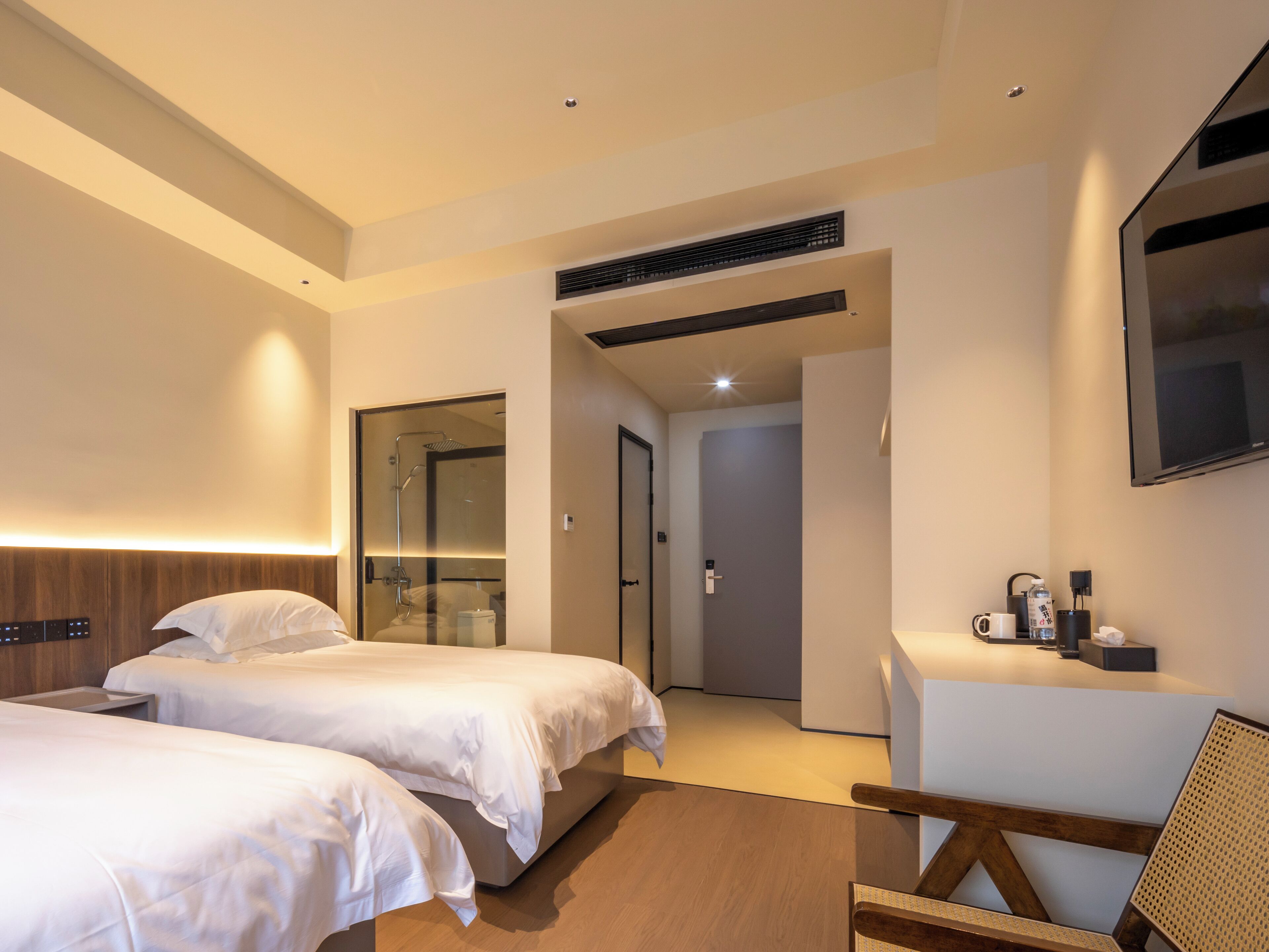 A hotel room with two beds, a desk, a chair, a TV, and a shower area.