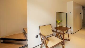 A modern hotel room with a wooden floor, a wooden chair with a woven seat, a small wooden table, and a mirror on the wall.