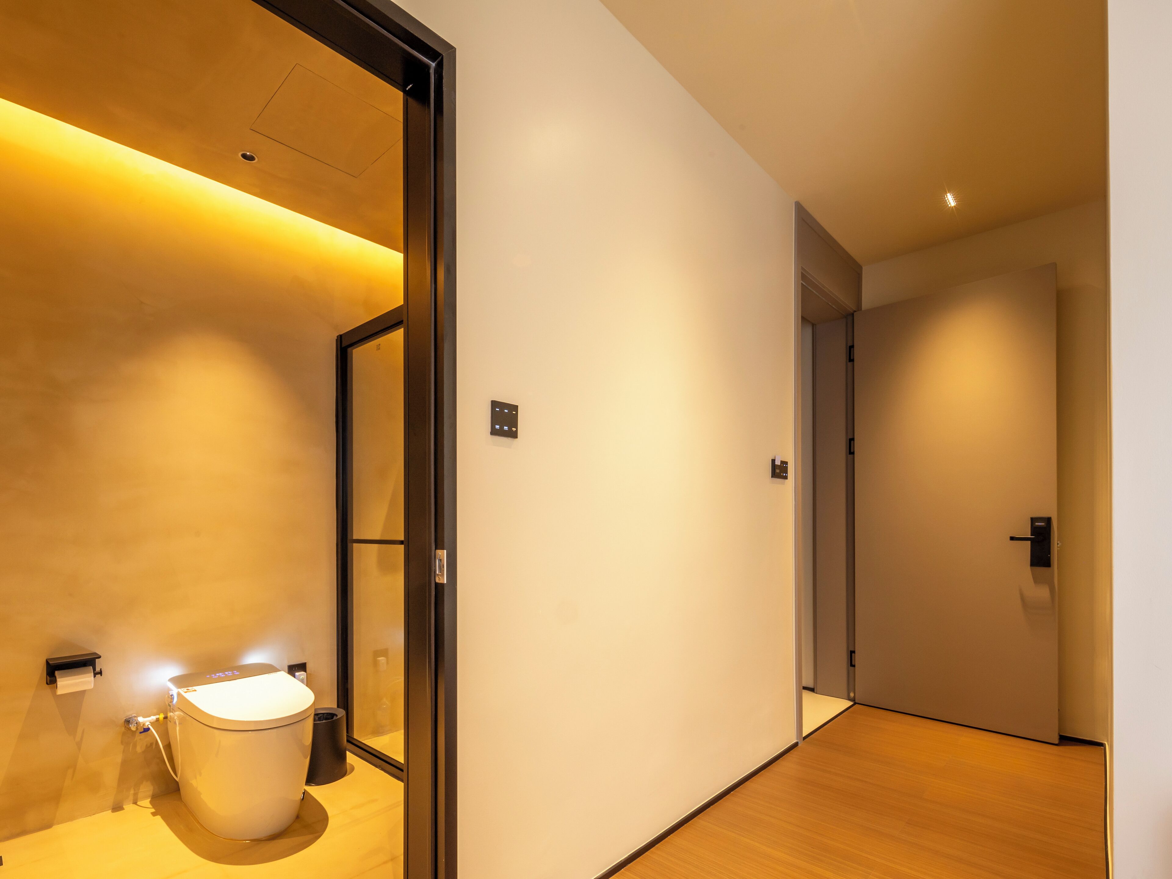 Un pasillo moderno de hotel con un inodoro, un cubo de basura y un interruptor de luz en la pared.