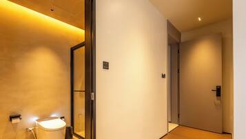 Un pasillo moderno de hotel con un inodoro, un cubo de basura y un interruptor de luz en la pared.