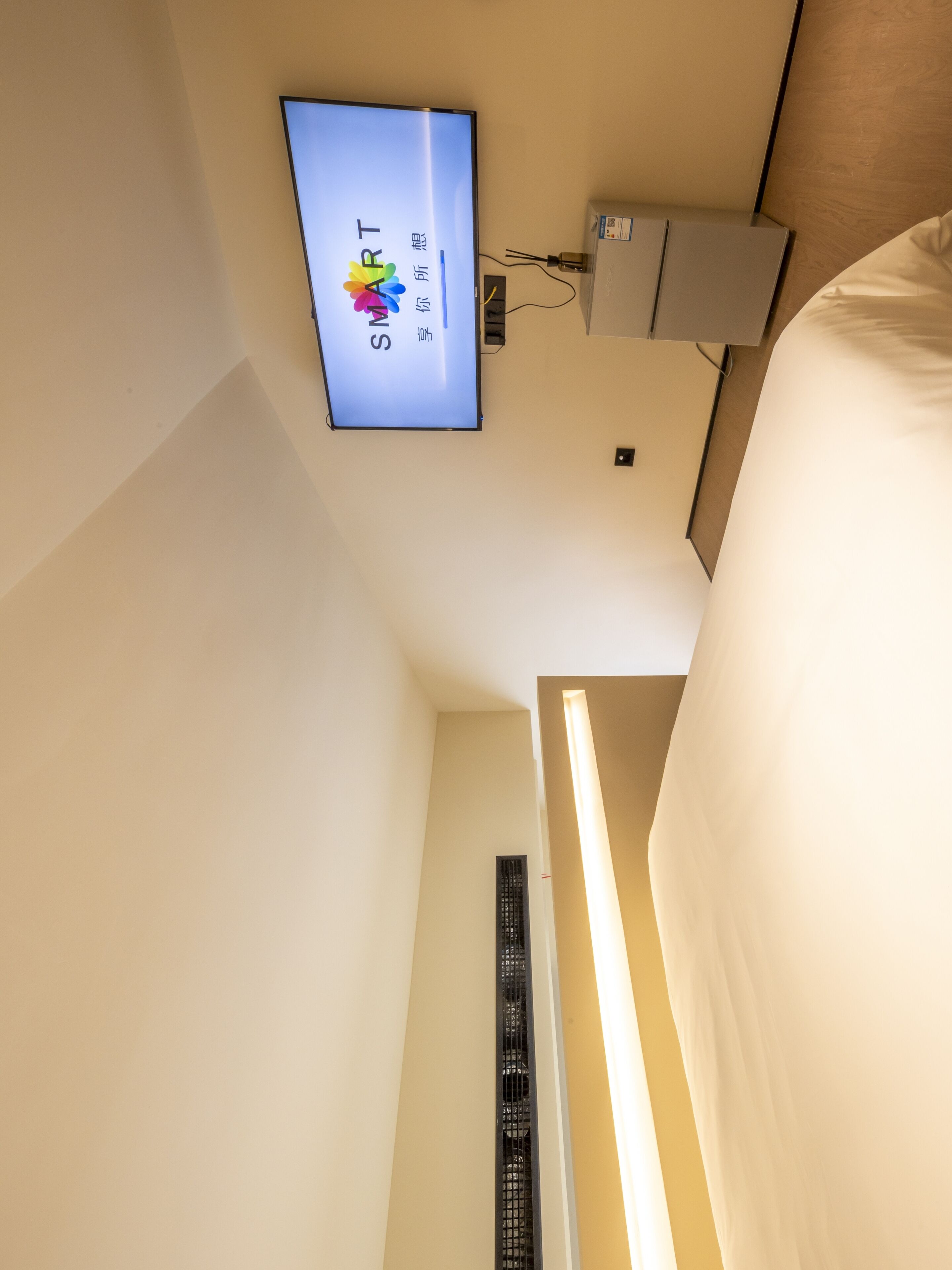 A hotel room with a bed, a TV mounted on the wall, and a thermostat.