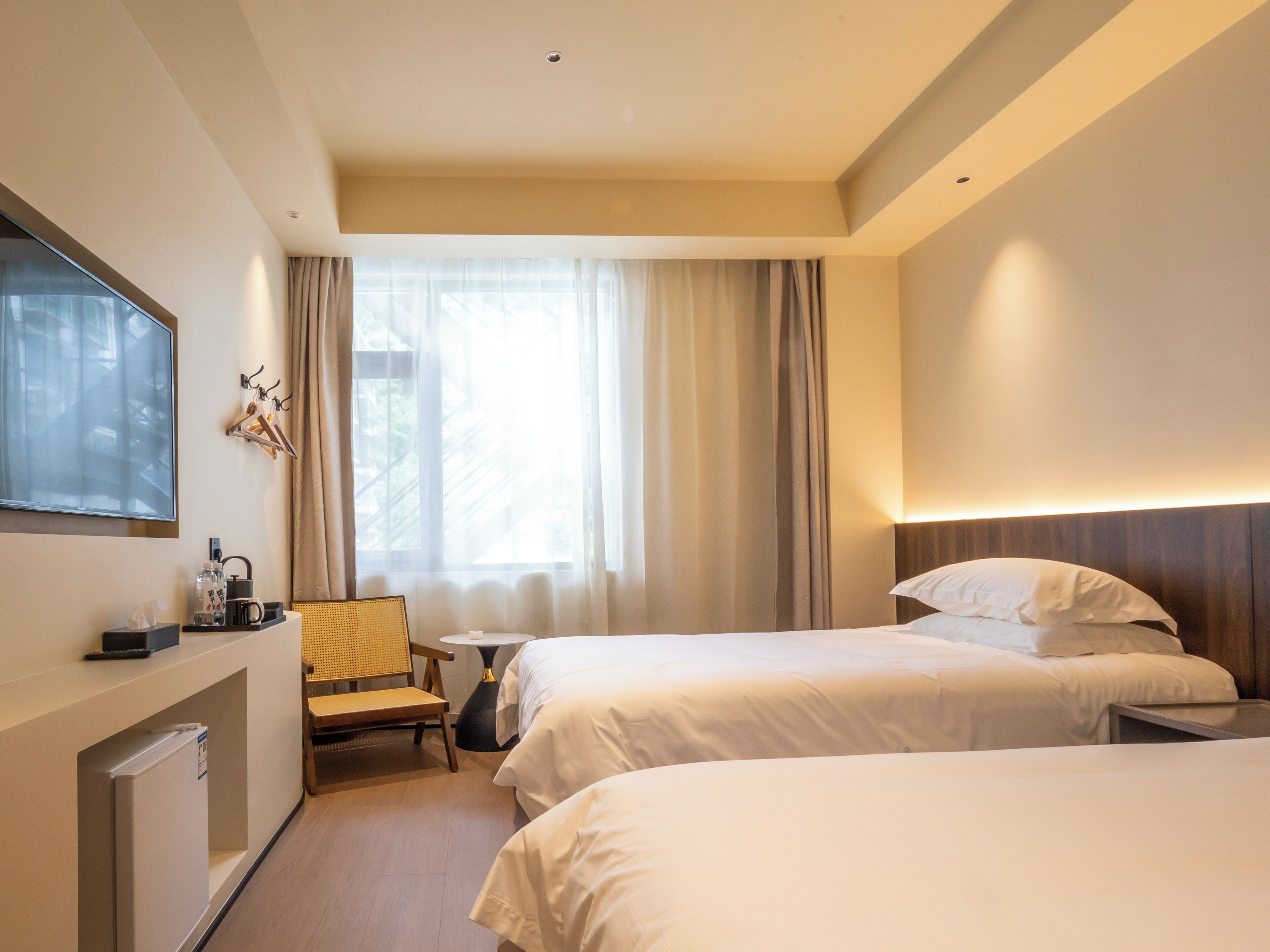 A hotel room with two beds, a desk, a chair, a TV, and a window with curtains.