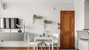 A modern living room with a white TV, grey cabinets, a wooden door, and a small table with two chairs.