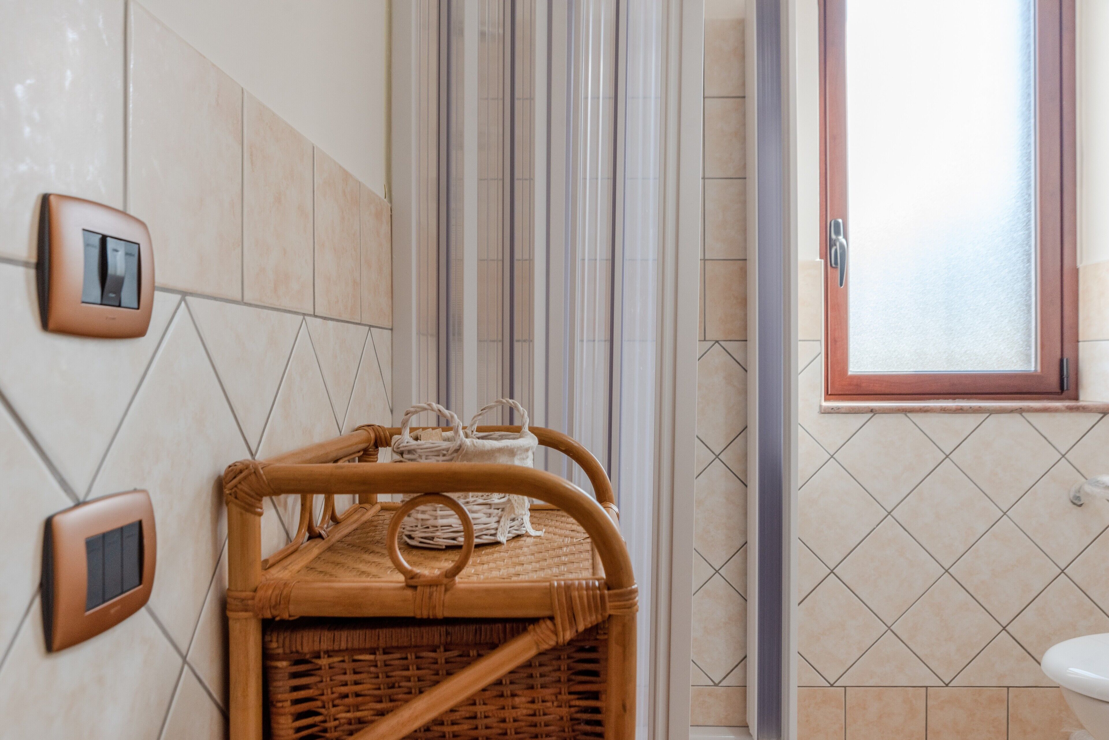 Un baño con una cesta de mimbre, una ventana y un termostato en la pared.