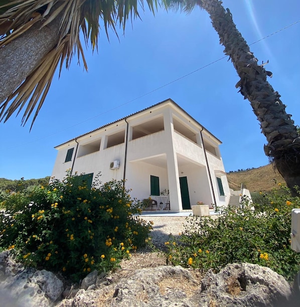 A two-story building with a balcony, surrounded by greenery and rocks.