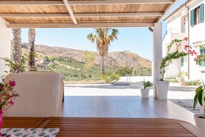 A covered outdoor seating area with a view of a mountainous landscape, potted plants, and a wooden table.
