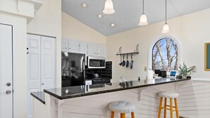 Una cocina moderna con armarios blancos, encimera negra y dos taburetes de madera.