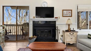 Una sala de estar con chimenea, televisor y vistas a árboles a través del ventanal corredera.