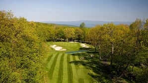 A golf course with sand bunkers, a water hazard, and a clear view of distant mountains.