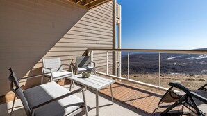 A balcony with a view of a mountainous landscape, furnished with a table, chairs, and a lounge chair.