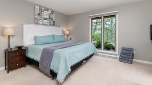 Ein Schlafzimmer mit Bett, Nachttischen, einem Fenster und Blick auf Grünflächen.