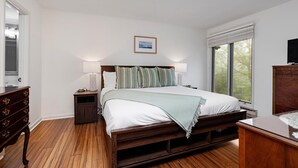 Une chambre à coucher avec un lit en bois, une table de chevet, une commode et une fenêtre avec des stores.