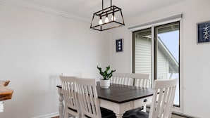Un coin repas avec une table en bois foncé et des chaises blanches, un luminaire suspendu et une plante en pot.
