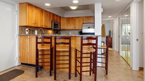 A kitchen with wooden cabinets, a microwave, a refrigerator, and a bar area with stools.