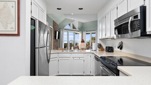 Una cocina moderna con armarios blancos, electrodomésticos de acero inoxidable y vistas amplias a través de grandes ventanales.