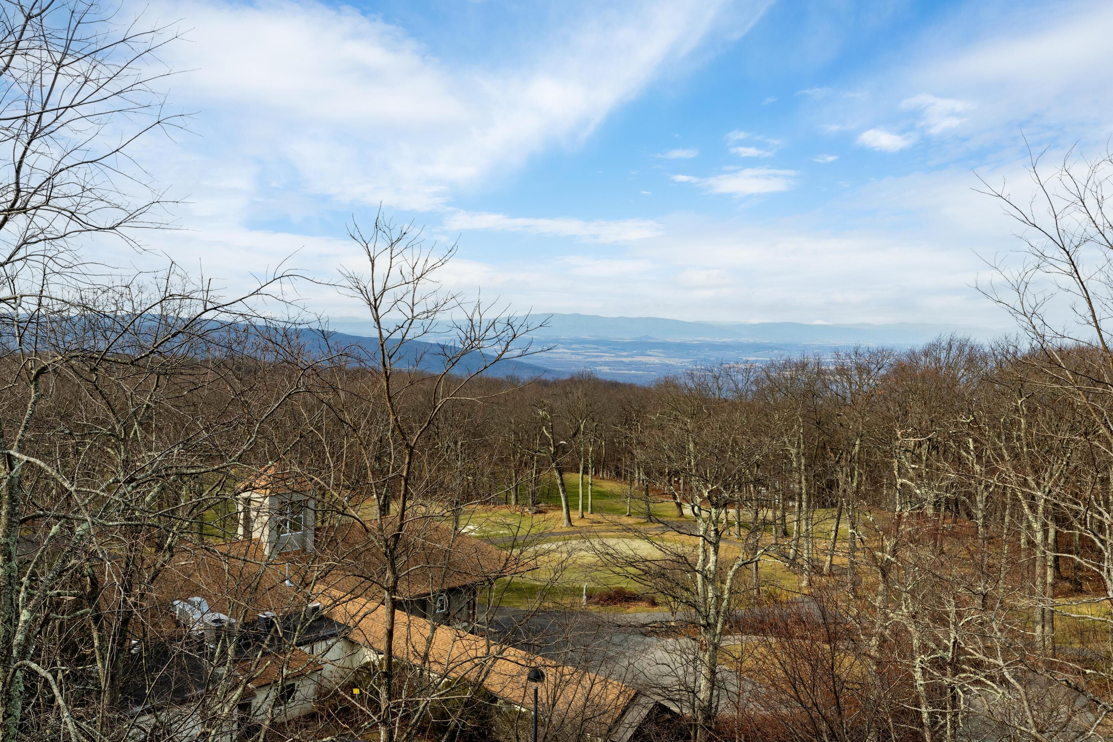 A rural landscape with a small building surrounded by trees and a distant view of mountains.