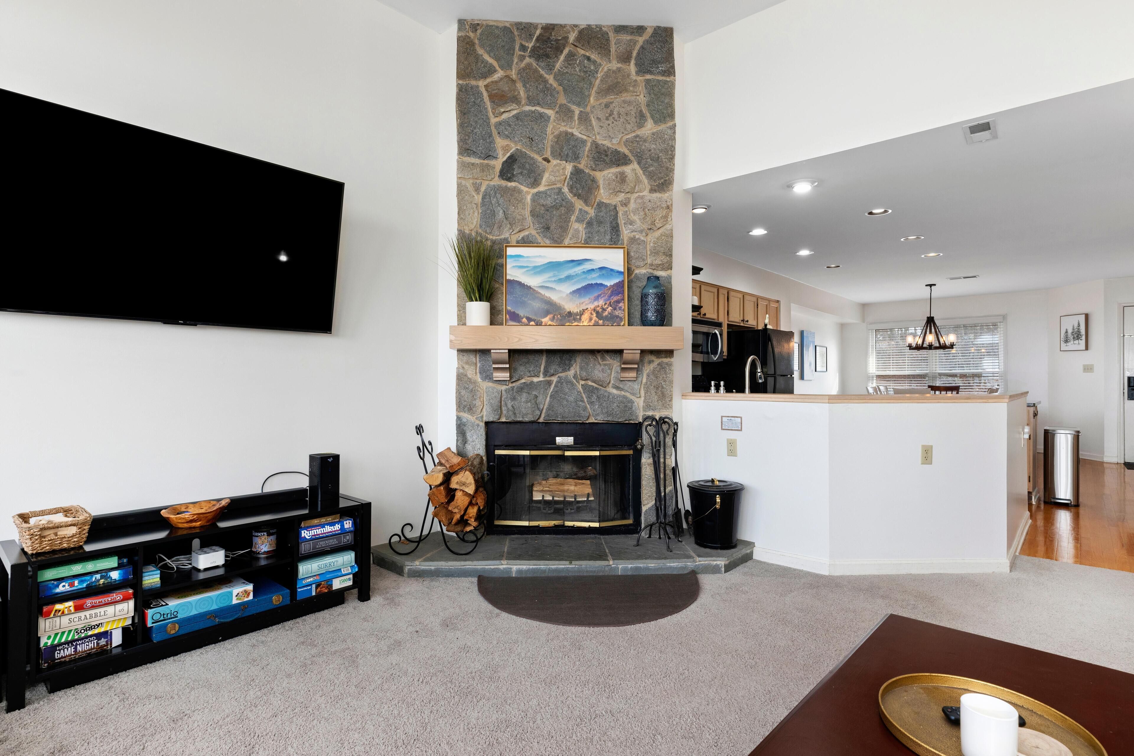 A modern living room with a stone fireplace, a flat-screen TV mounted on the wall, and a built-in entertainment unit with board games.