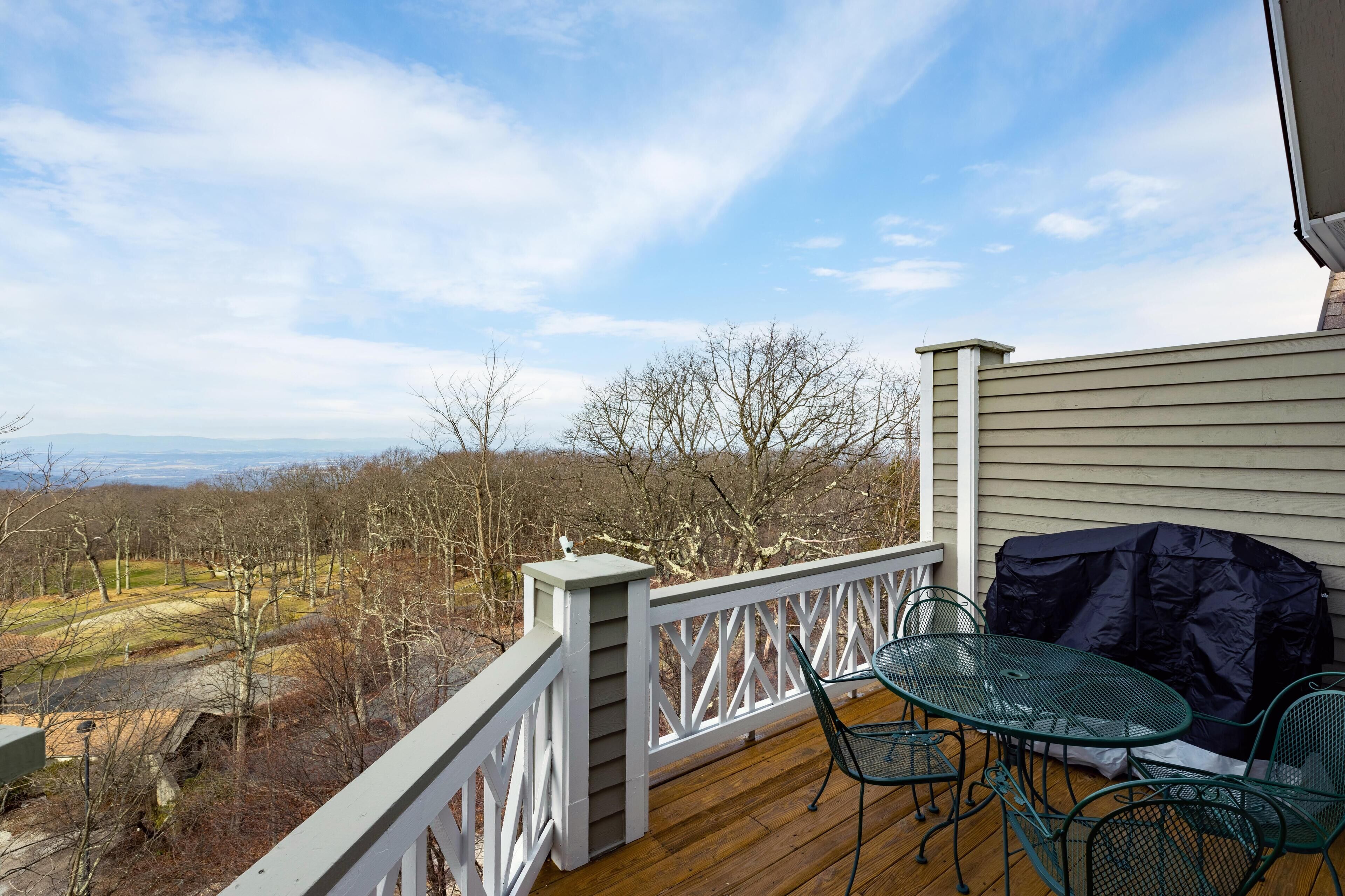 Une terrasse en bois avec une balustrade blanche, un barbecue couvert et une table avec des chaises.