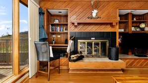 A spacious living room with a fireplace, wooden bookshelves, and a large window overlooking a deck.