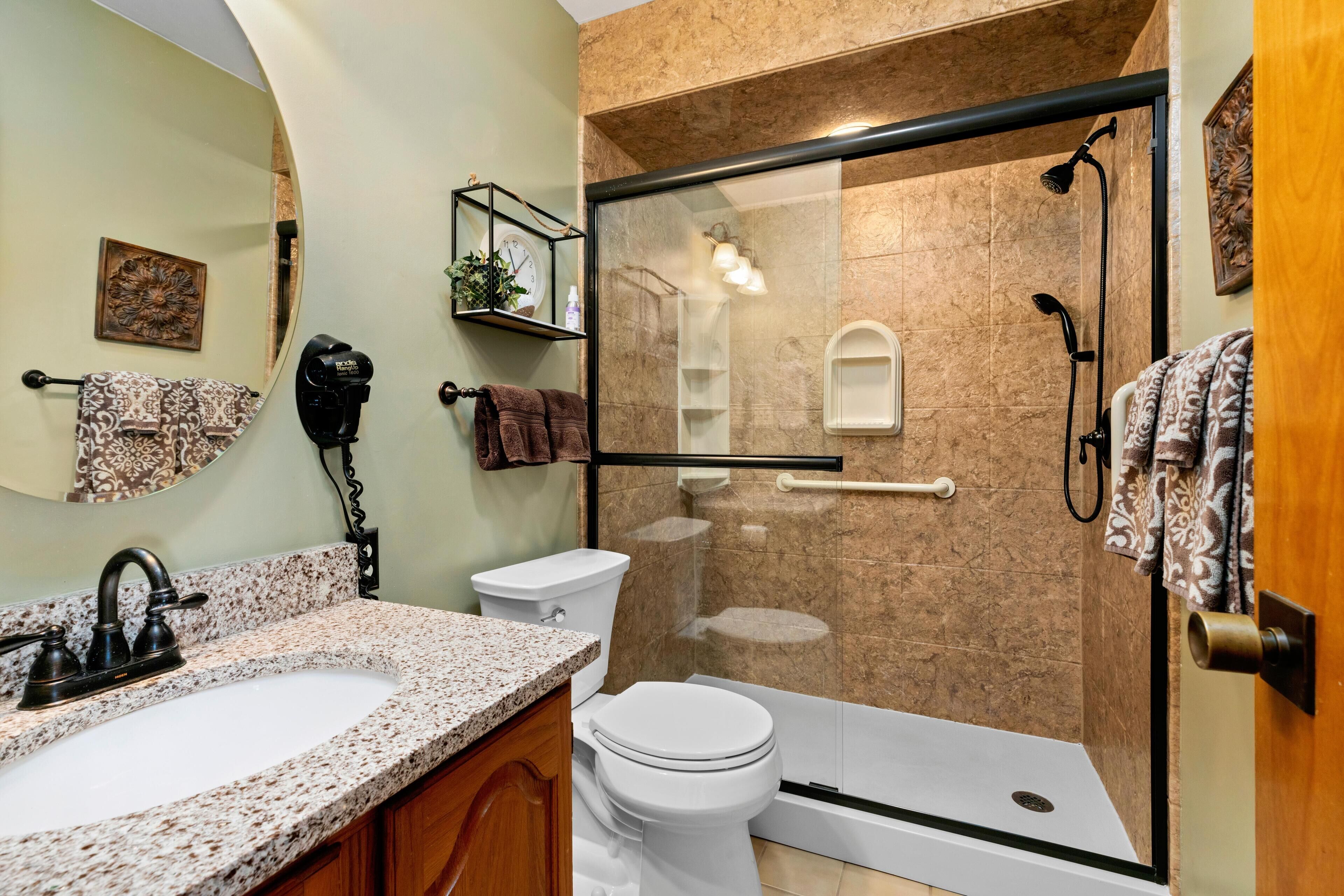 A bathroom with a granite countertop sink, a toilet, a glass-enclosed shower, and a wooden cabinet.