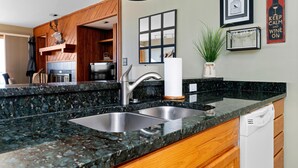 A kitchen with a granite countertop, stainless steel sink, and wooden cabinets.