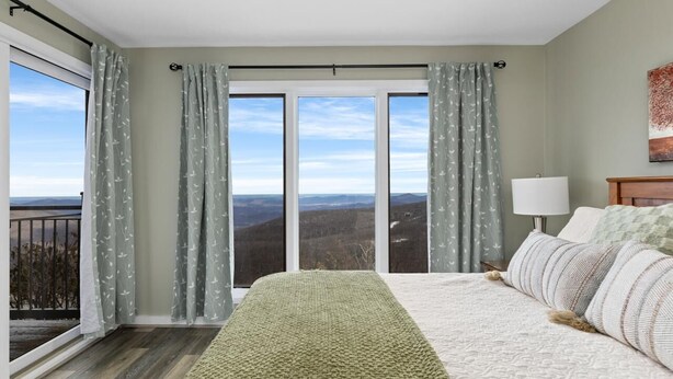 Un dormitorio con una cama grande, una mesita de noche, una lámpara y vistas al exterior a través de una puerta corrediza de vidrio.