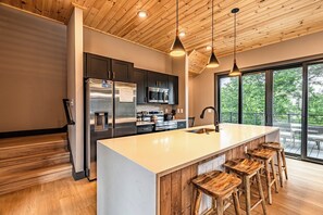 Une cuisine moderne dotée d’un grand îlot central, d’appareils électroménagers en acier inoxydable et de tabourets de bar en bois.