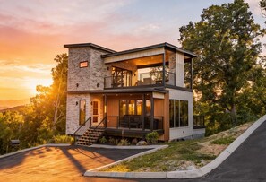 Une maison moderne à deux étages, dotée d’une façade en pierre, d’un balcon, d’un design contemporain et d’une allée.