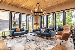 A spacious living area with large windows, a chandelier, and a leather armchair. - Serene Cabin Retreat・Rooftop Deck・Hot Tub・Games (Sevierville)