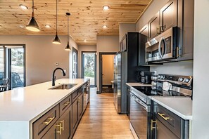 A modern kitchen with a central island, stainless steel appliances, and a wooden ceiling.