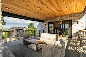 A covered outdoor area with wicker furniture, a wooden ceiling, stone walls, and a view of the landscape.