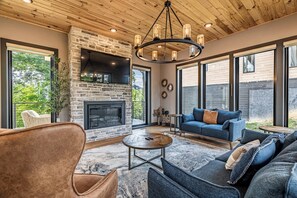 A modern living room with a stone fireplace, large windows, and a cozy seating area.