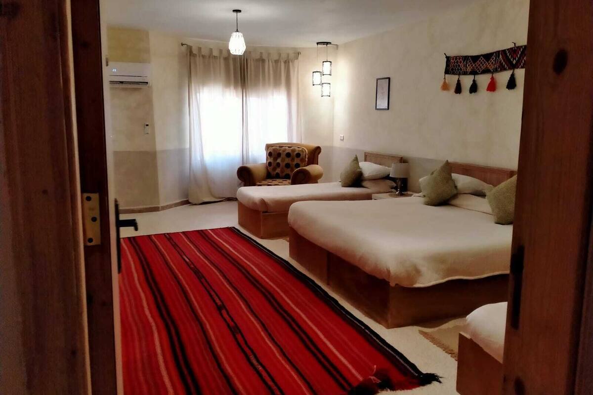 A hotel room with two beds, a red striped rug, a wooden chair, and a ceiling light.
