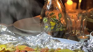 A table with foil-wrapped food, a glass bottle with a plant design, and a lit candle in the background. - b&b petrafarmhouse  (Wadi Musa)
