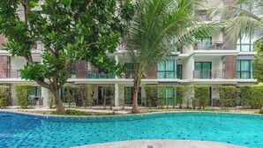 Una piscina con borde de azulejos, rodeada por un edificio con balcones y árboles.