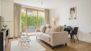 A modern living room with a beige sofa, a glass coffee table, and a dining area with a table and chairs. - Modern 2-Bed flat in Mill hill Park (London)
